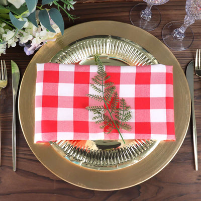 Red and white checked napkin on a gold charger plate with greenery