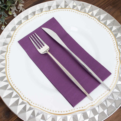 Elegant silver fork and knife on a purple napkin atop a decorative plate.