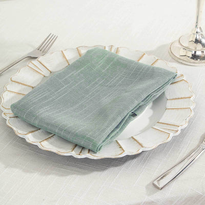 Folded green napkin on a decorative plate with silver cutlery.