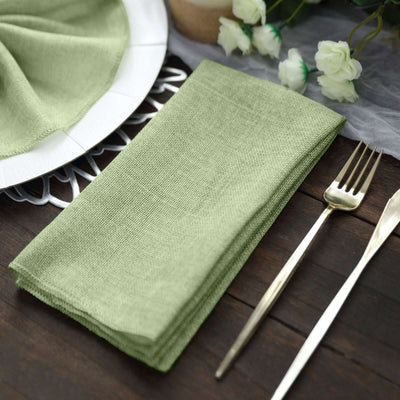Green linen napkin neatly folded on a wooden table with cutlery and flowers.
