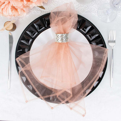 Peach tulle napkin tied with a silver ring on a black decorative plate.