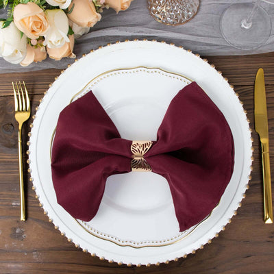 Burgundy napkin with gold holder on elegant dinner plate, styled table setting.
