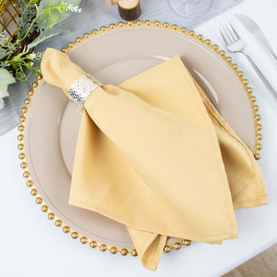 Gold napkin on a decorative plate with beaded edge on a beautifully set table.