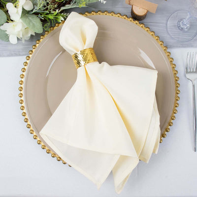 Elegant cream napkin with gold ring on a stylish dinner plate setting.