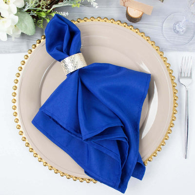Blue napkin with silver ring on a decorative plate, elegantly arranged for dining.