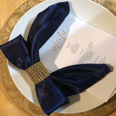 Navy satin napkin with jeweled ring on a decorative plate and menu card.