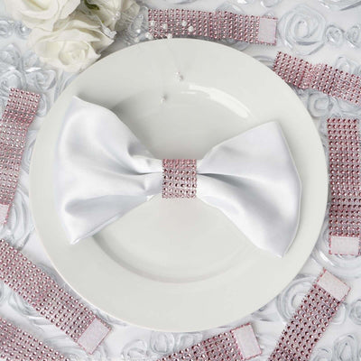White satin bow with rhinestone embellishment on a plate, surrounded by pink rhinestone strips.