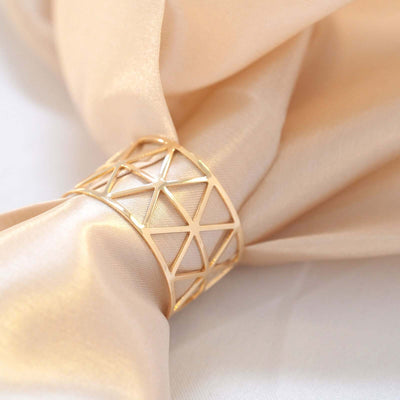 Gold geometric napkin ring on a soft fabric background.