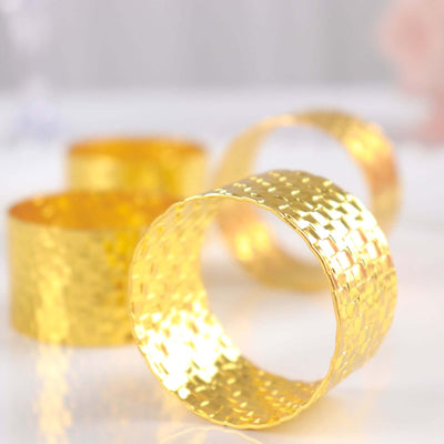 Gold woven napkin rings on a reflective surface.