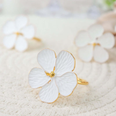 White flower ring with gold accents on a textured surface.