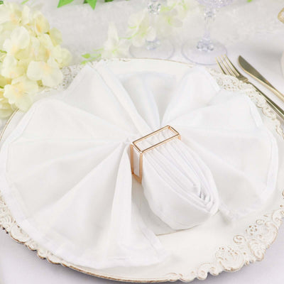 Elegant white napkin elegantly folded and secured with a gold ring on a decorative plate.