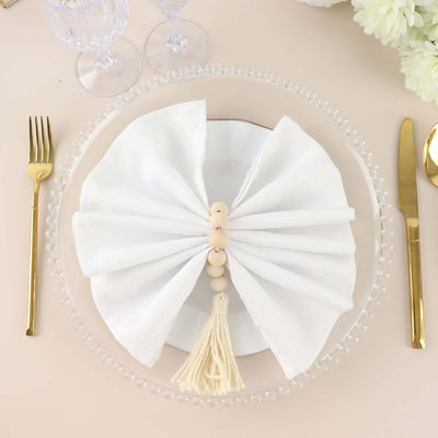 White napkin elegantly arranged on a plate with decorative beads and tassel.