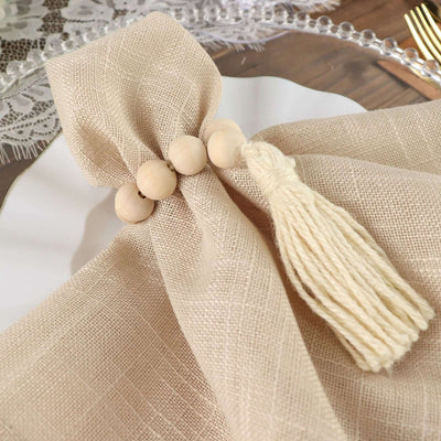 Beige linen napkin with wooden beads and tassel on a white plate.