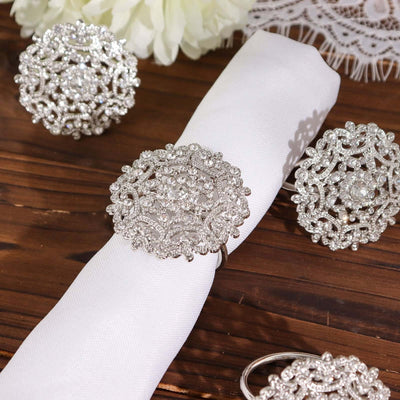 Silver decorative napkin rings with intricate designs on a wooden table.