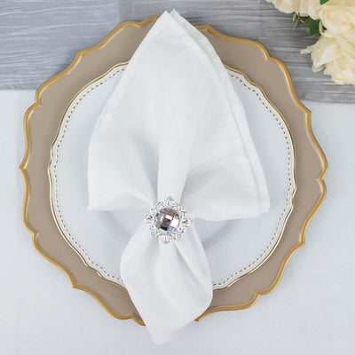 Elegant white napkin with jeweled ring on a decorative plate.