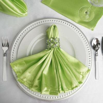 Green satin napkin with jeweled ring on a plate setting.
