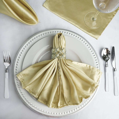 Elegant gold satin napkin with crystal ring on a decorative plate setting.