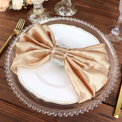 Elegant gold satin napkin bow on a clear plate with beaded edge.
