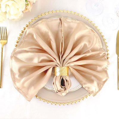 Elegant folded beige napkin with gold ring on decorative plate.