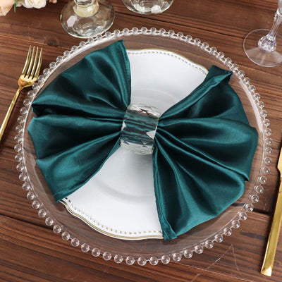 Teal satin napkin bow on a clear plate atop a wooden table.
