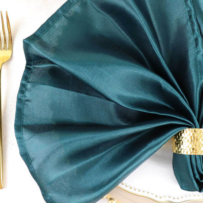 Teal satin napkin elegantly arranged with a gold ring on a dining plate.