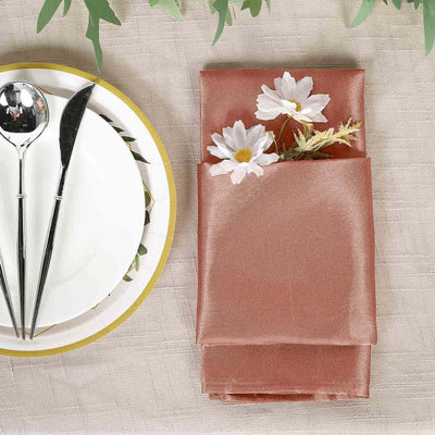 Rose satin napkin with flowers, silver cutlery, and decorative plate on a table setting.