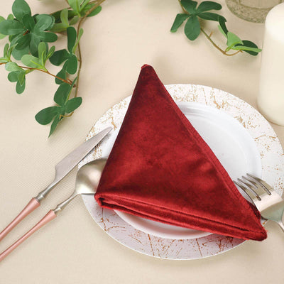 Red velvet napkin on a decorative plate with cutlery and greenery.