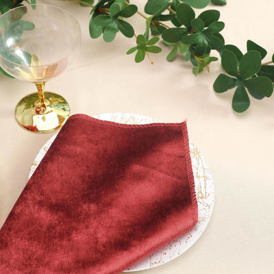 Burgundy velvet napkin on a decorative plate with greenery in the background.
