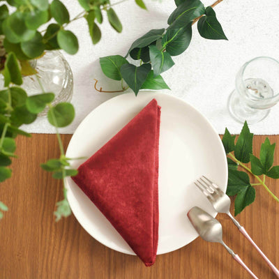 Red velvet napkin neatly folded on a white plate, surrounded by greenery.