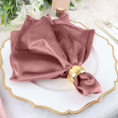 Dusty rose napkin elegantly wrapped with a gold napkin ring on a decorative plate.