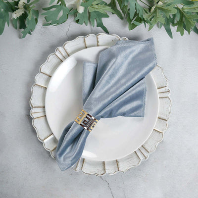 Elegant blue napkin with a decorative ring on a white plate, styled with greenery.