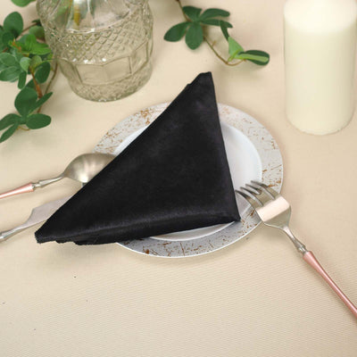 Black cloth napkin elegantly folded on a decorative plate with utensils.