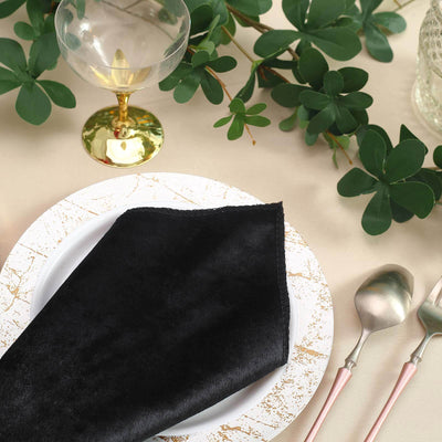 Elegant black napkin on a decorative plate with gold accents, surrounded by greenery.