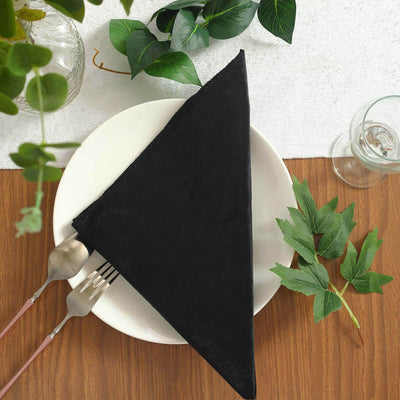 Black triangle napkin elegantly placed on a white plate with greenery accents.