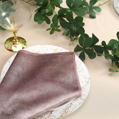 Rose gold napkin on a decorative plate with greenery and a glass.