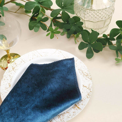 Navy blue napkin on a decorative plate with greenery and glassware.