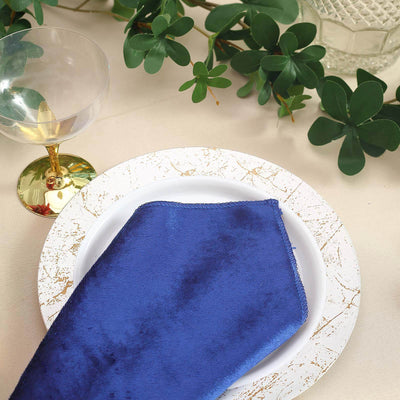 Elegant blue napkin on a decorative plate with greenery and glassware in a table setting.