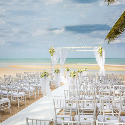 Beach wedding setup with chairs, altar, and floral decor by the sea.