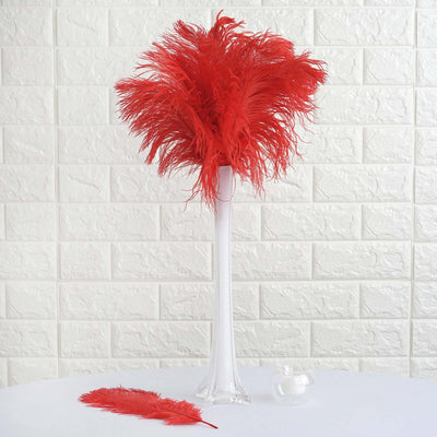 Red feather centerpiece in a clear vase with a feather beside it.