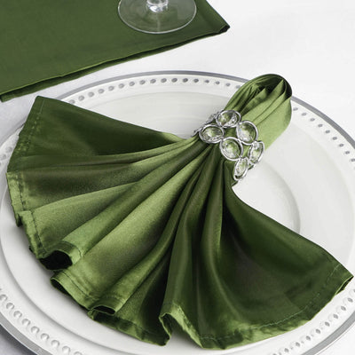 Green satin napkin elegantly arranged with a jeweled napkin ring on a white plate.