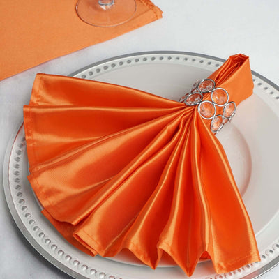 Elegant orange satin napkin with jeweled napkin ring on a white plate.