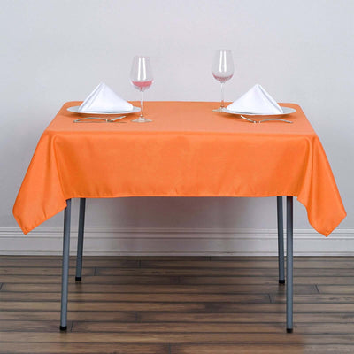 Orange tablecloth on a dining table set with glasses and napkins.