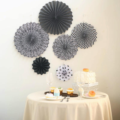 Black and white decorative paper fans on wall above a dessert table.