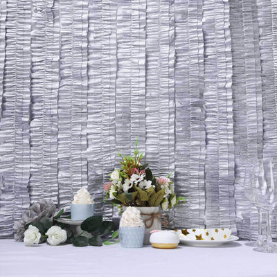 Decorative table setting with flowers, desserts, and glassware against textured backdrop.