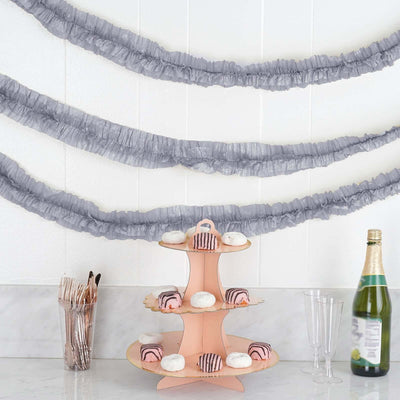Pink tiered cake stand with pastries, gray ruffled garlands in background.