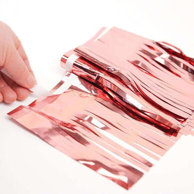 Hand holding rose gold fringe decoration strips on a white background.