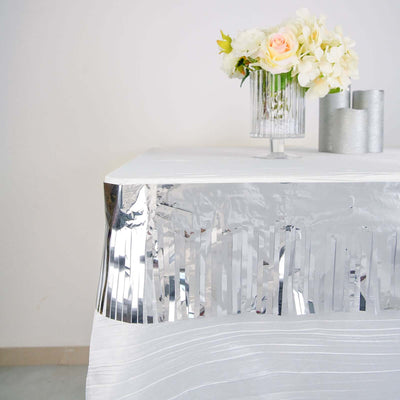 Silver fringed table skirt with floral centerpiece and decorative vases.