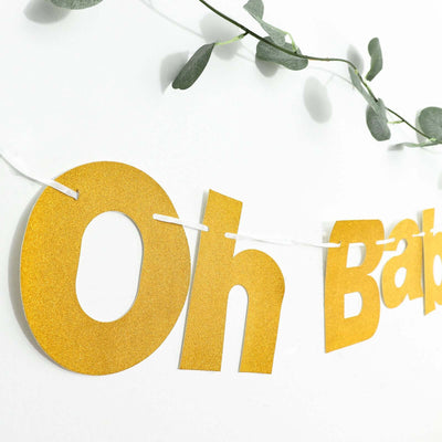 Gold "Oh Baby" banner with greenery against a white background.