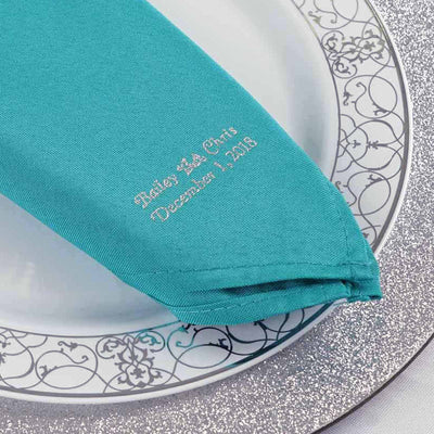 Embroidered teal napkin on a decorative plate for special occasions.