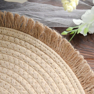 Natural woven round jute rug with fringe detail on wooden surface.